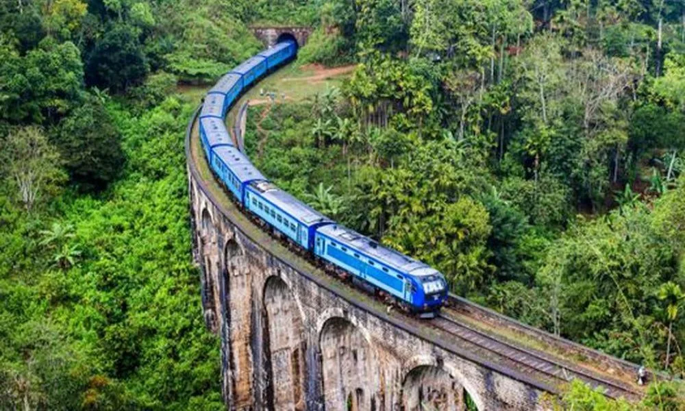 Blue passenger train winding through lush tea plantations between Kandy and Ella