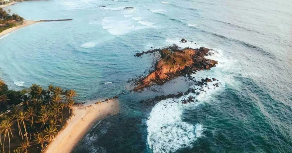 Aerial view of Parrot Rock outcrop and connecting sandbar in Mirissa Bay